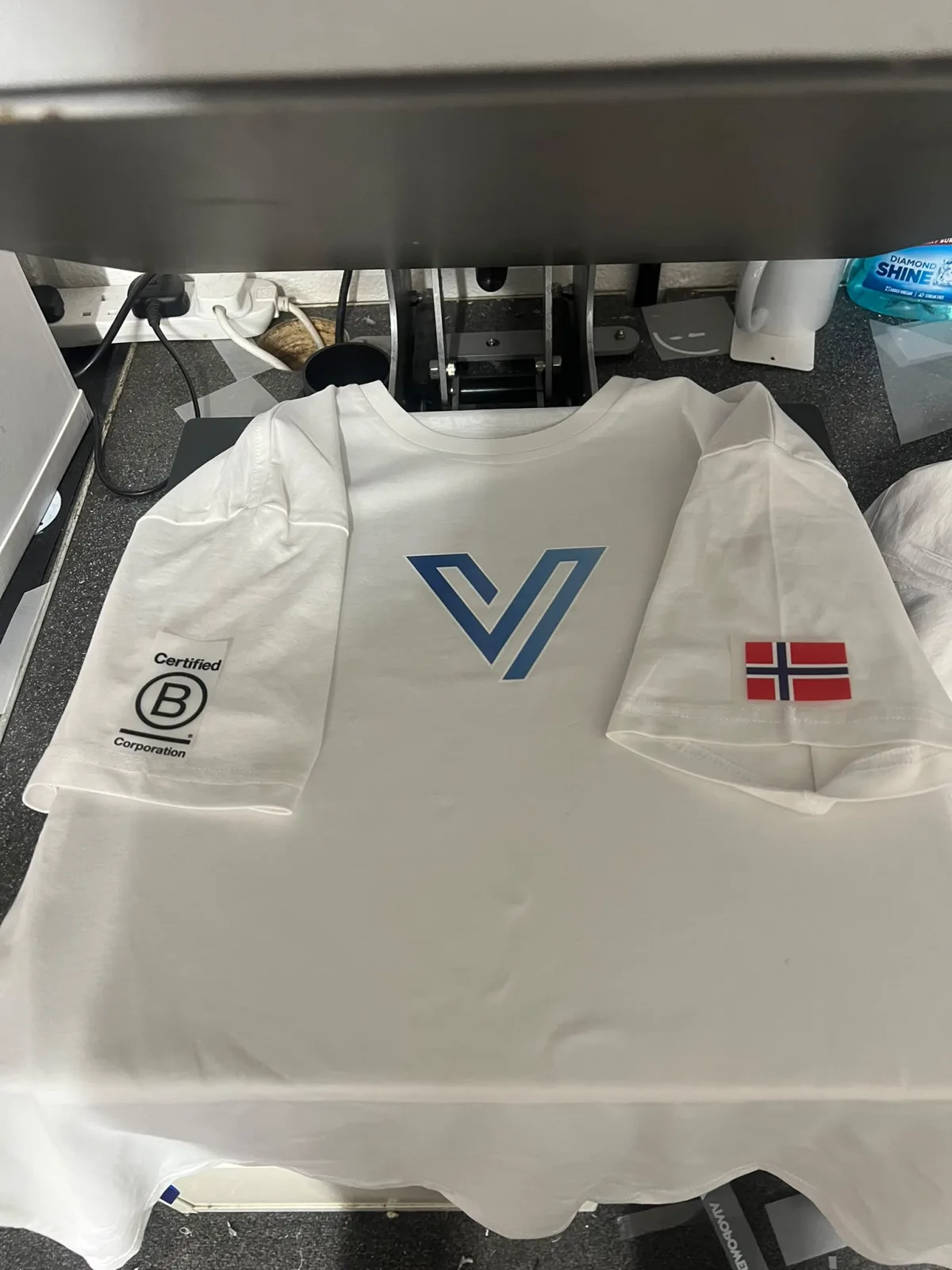 White premium cotton T-shirt on the heat press with a blue two-colour logo print on the chest and small prints on both sleeves